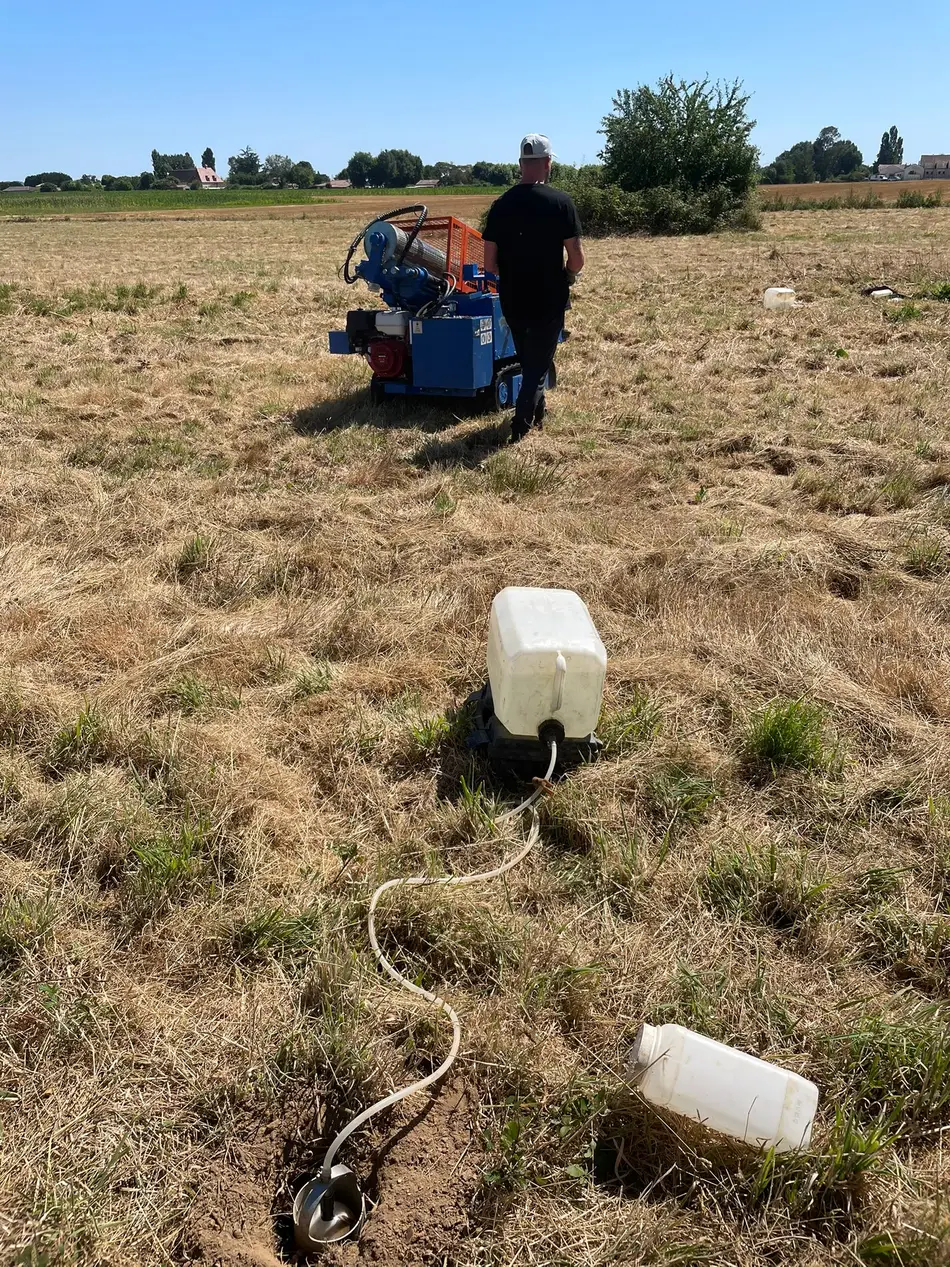 Test de perméabilité (méthode Porchet) : bidons d'eau reliés à des trous de mesure sur un terrain à bâtir.